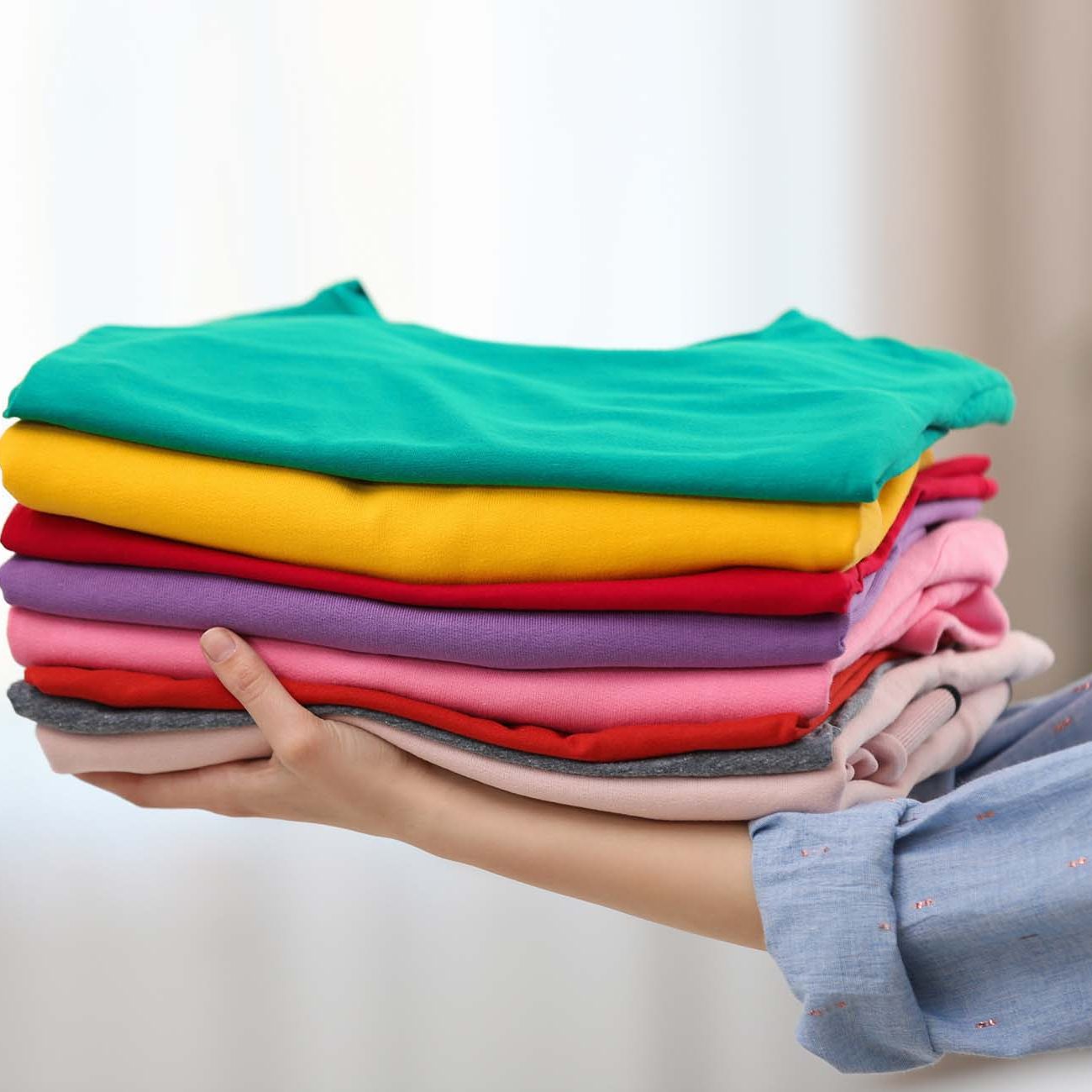 Woman holding folded clean clothes indoors, closeup. Laundry day